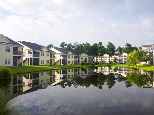 Several low-rise multifamily residential buildings with exterior staircases line a pond.