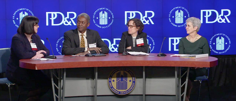 Image showing four individuals, panelists Erika Poethig, Raphael Bostic, Ingrid Gould Ellen, and Margery Turner seated at a table bearing the HUD logo. An image with the HUD and PD&R logos is visible on a screen behind the table.